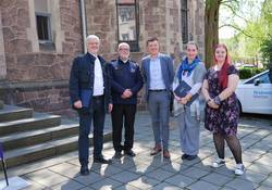 5 Personen vor Treppenstufen und einer Kirche stehen auf grauem Untergrund