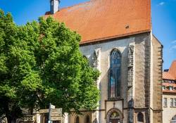 Hellbraune Fassade und rotes Ziegeldach des Stadtmuseums mit grünem Blattwerk daneben und blauem Himmel im Hintergrund