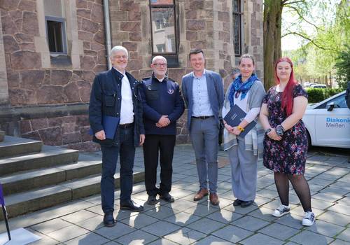 ESF-Fördermittel für Diakonie Meißen und Lebensfahrten e. V. © Stadt Meißen 5 Personen vor Treppenstufen und einer Kirche stehen auf grauem Untergrund