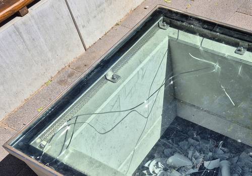 Vandalismus an der Porzellan-Schaufläche in Meißen © Stadt Meißen Hellblaue Glasscheibe mit Riss, darunter Porzellanscherben und hellbrauen Steinen an der linken Seite