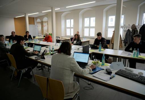 Menschen um einen großen Tisch mit Laptops und Unterlagen