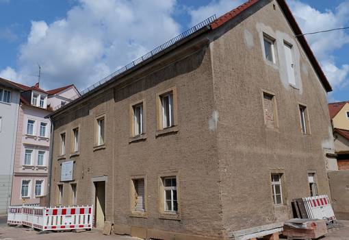 Gebäude mit Bauzaun rechts vor blauem Himmel mit Wolken