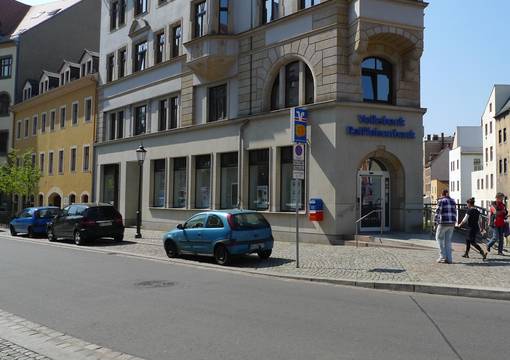 Straße mit parkenden Autos und Passanten
