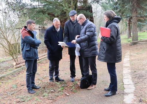 Gruppe von einer Frau und drei Männern steht auf einem Parkweg und betrachtet gemeinsam einen Plan