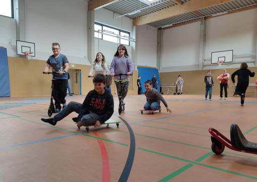 Kinder fahren auf Rollerfahrzeugen in einer Sporthalle