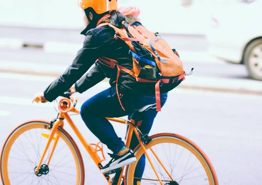 Fahrradfahrer fährt auf orangenem Rad mit Helm und Rucksack nach links