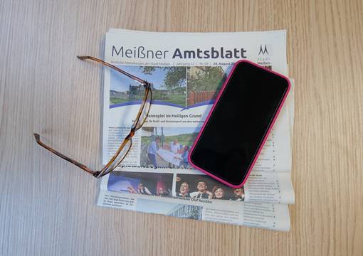Handy und Brille liegen auf Zeitungen auf braunem Holz