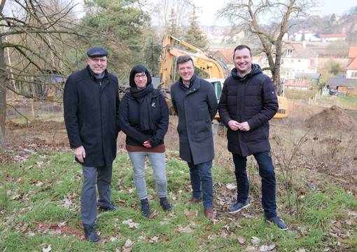Fröhliche Menschen in Winterkleidung vor Baufeld im Grünen