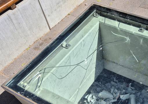 Hellblaue Glasscheibe mit Riss, darunter Porzellanscherben und hellbrauen Steinen an der linken Seite