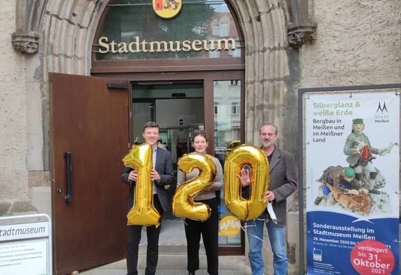 Bürgermeister Markus Renner, Museumsleiterin Linda Karohl-Kistmacher und Museumsmitarbeiter Steffen Förster mit Zahlenluftballons 1,2 und 0 vor der Tür des Stadtmuseums