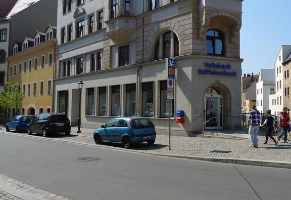 Straße mit parkenden Autos und Passanten