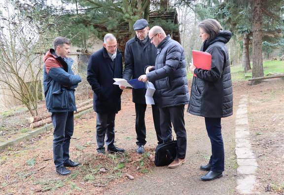 Gruppe von einer Frau und drei Männern steht auf einem Parkweg und betrachtet gemeinsam einen Plan