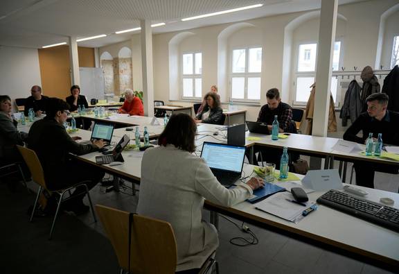 Menschen um einen großen Tisch mit Laptops und Unterlagen