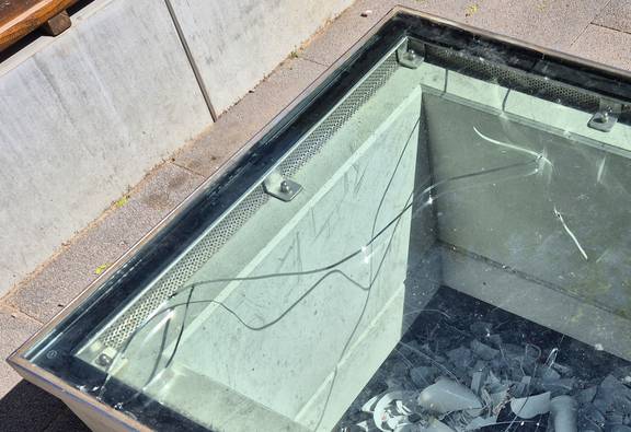 Hellblaue Glasscheibe mit Riss, darunter Porzellanscherben und hellbrauen Steinen an der linken Seite